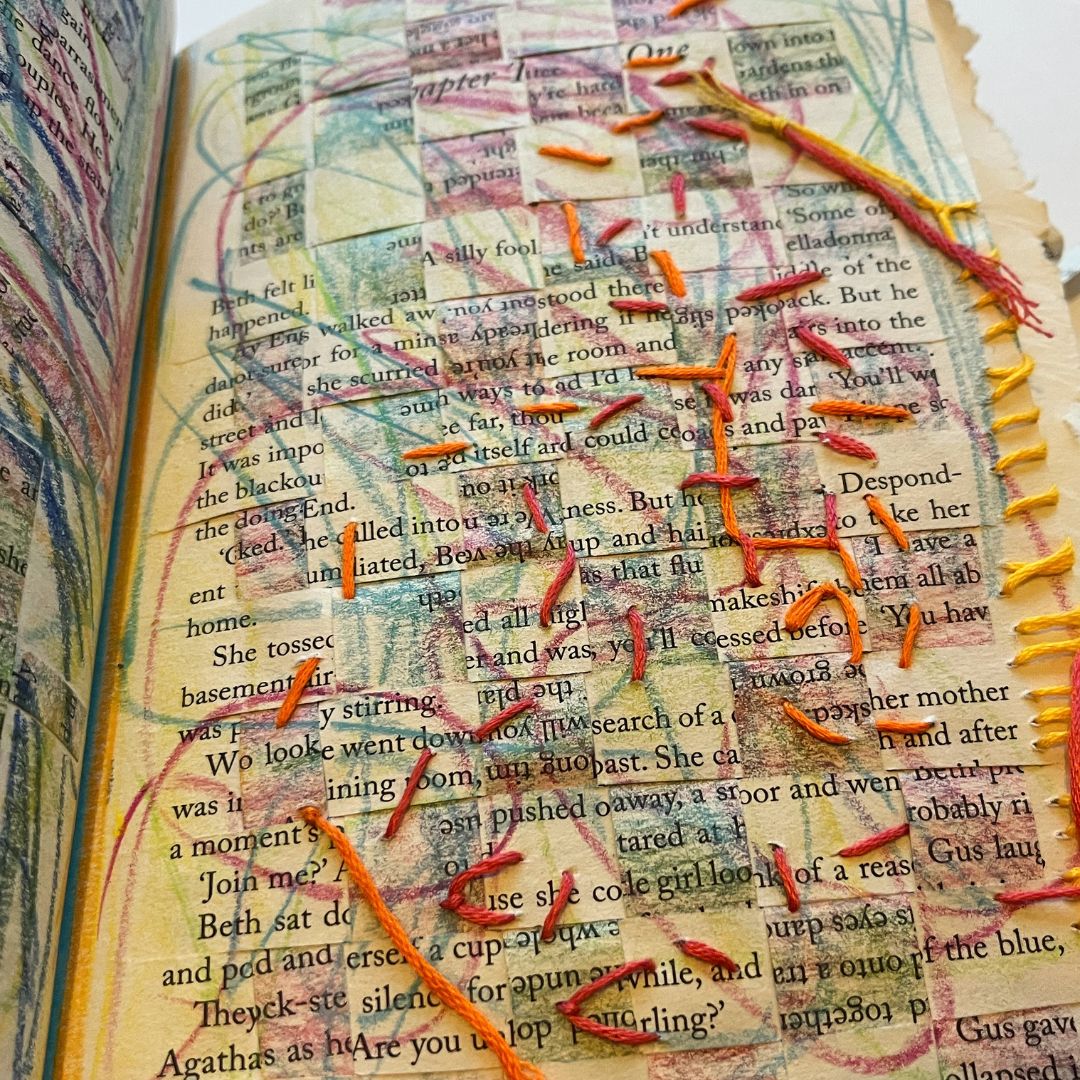 A book that has been used for arts and crafts. It has been cut up into a collage and some of the pieces are coloured in with crayons. There are bits of string stuck on it with glue.