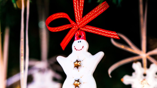 A festive snowman decoration hanging from a Christmas tree with red ribbon.