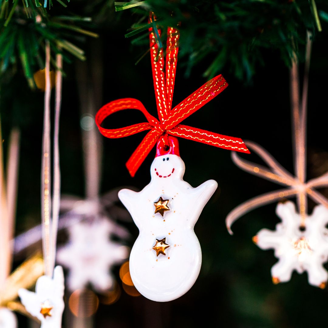 A festive snowman decoration hanging from a Christmas tree with red ribbon.