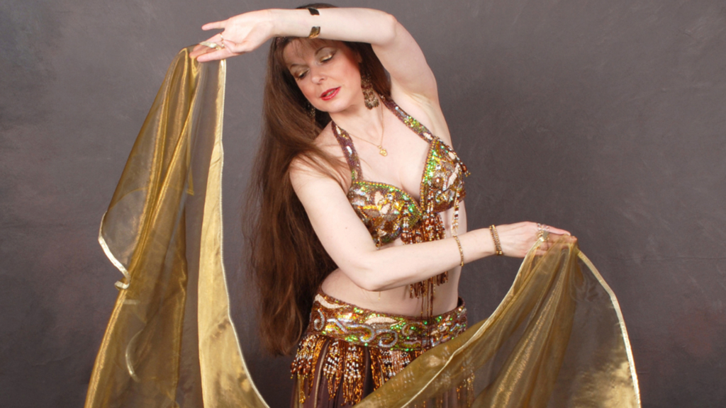 A bellydancer wearing a glamorous outfit full of sequins and holding a sheer gold sheet.