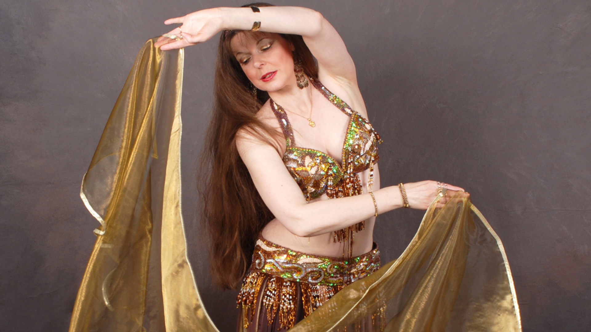 A bellydancer wearing a glamorous outfit full of sequins and holding a sheer gold sheet.