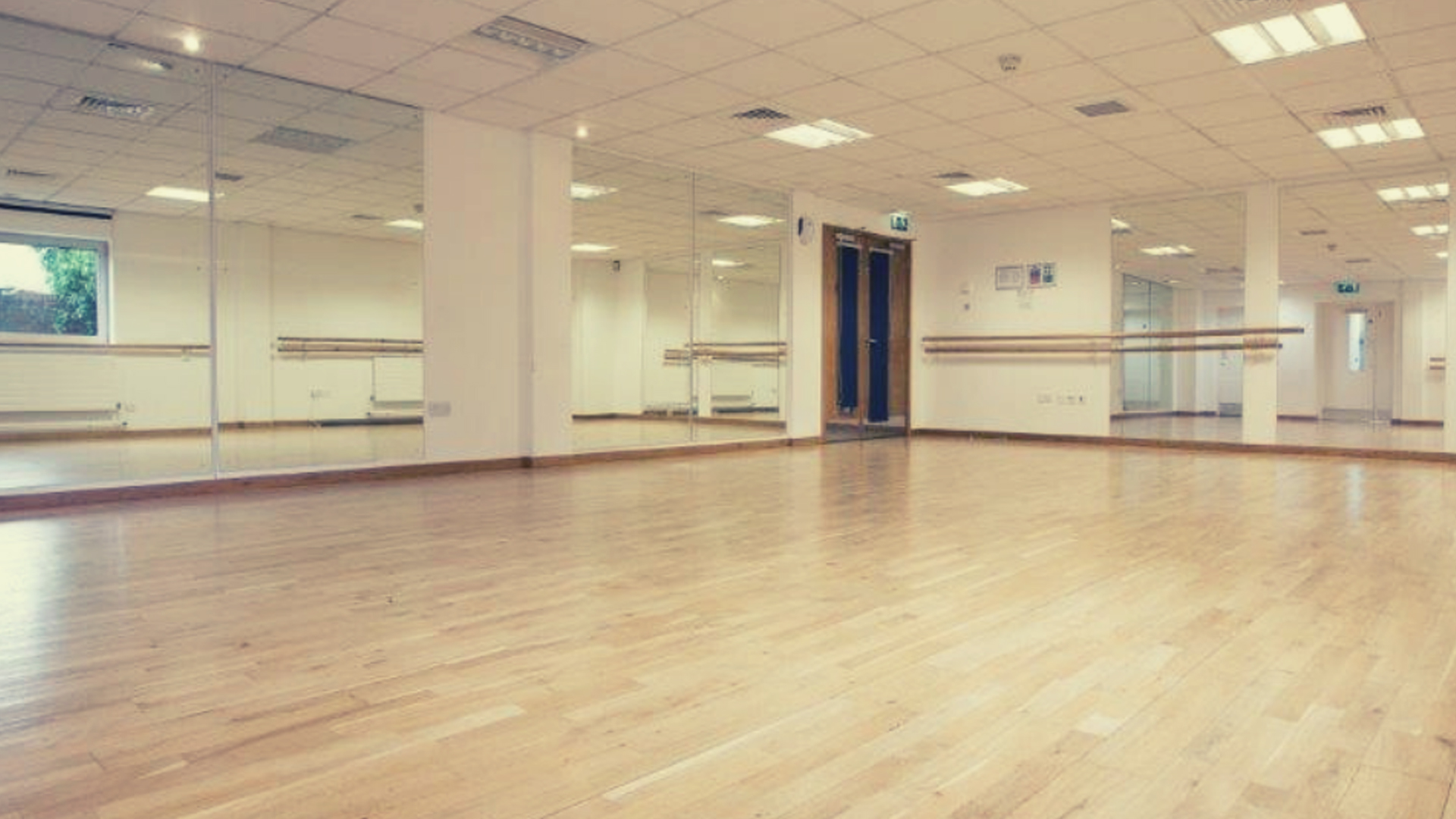 A studio space with laminate floors and a mirrored wall with a barre.