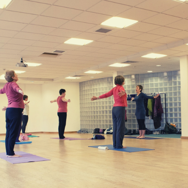 A group of people in a yoga class stood on their yoga mats alongside their yoga teacher.