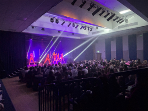 A Taylor Swift tribute act performing on stage in a red sequined outfit with back-up dancers and a big crowd watching them.