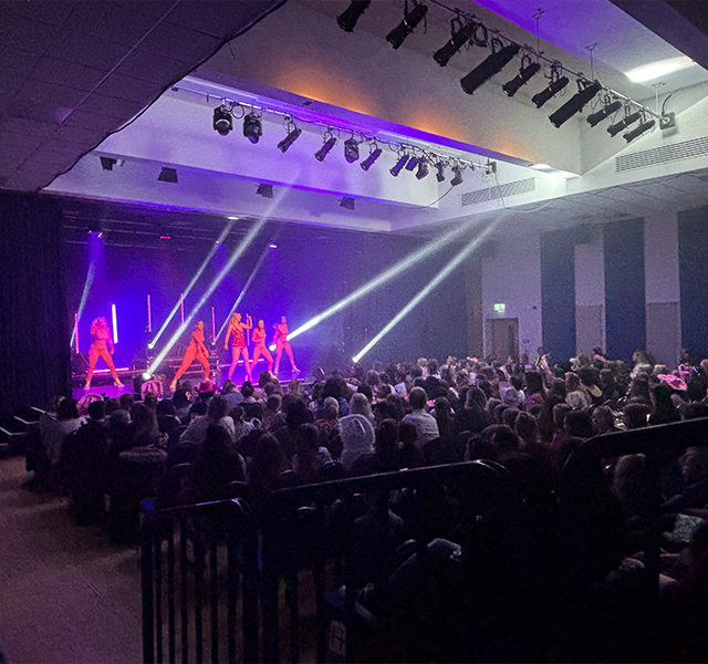 A Taylor Swift tribute act performing on stage in a red sequined outfit with back-up dancers and a big crowd watching them.